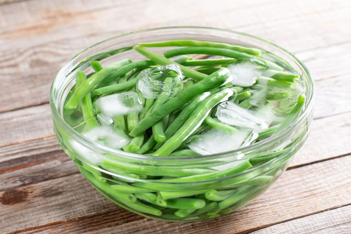 french green beans with shallots recipe, Green beans in a colander Boiled or blanched vegetables in ice water on a wooden table