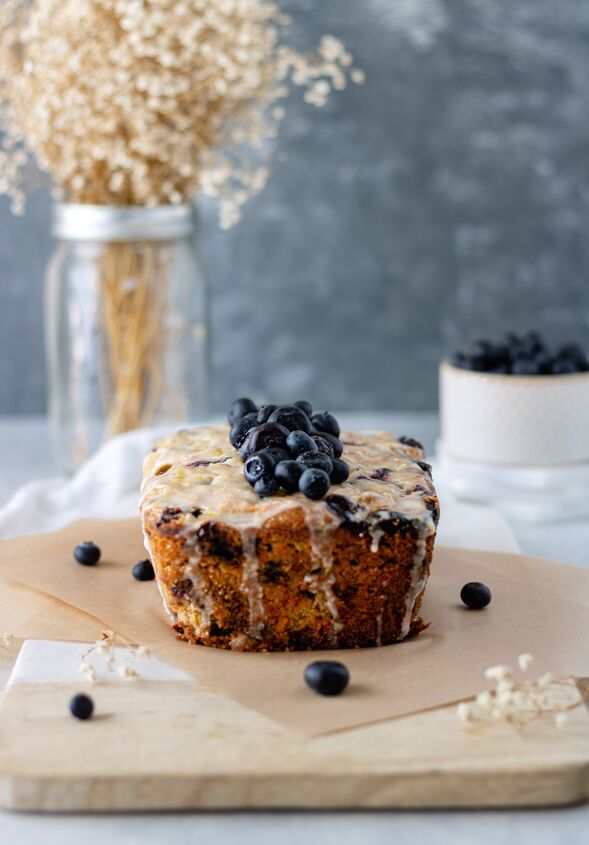 Lemon Blueberry Zucchini Bread with Lemon Glaze sitting on a marble cutting board and surrounded by baby s breath and blueberries
