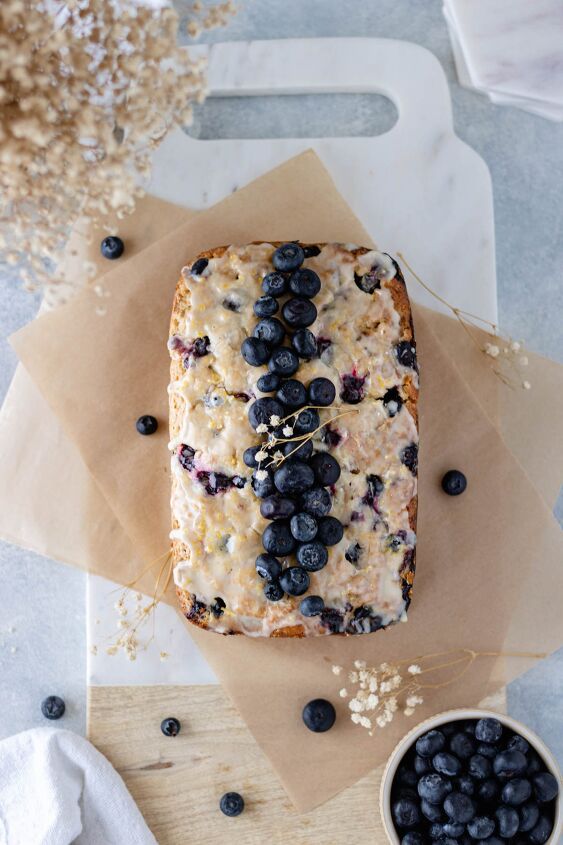 Lemon Blueberry Zucchini Bread with Lemon Glaze on parchment paper and topped with fresh blueberries and baby s breath