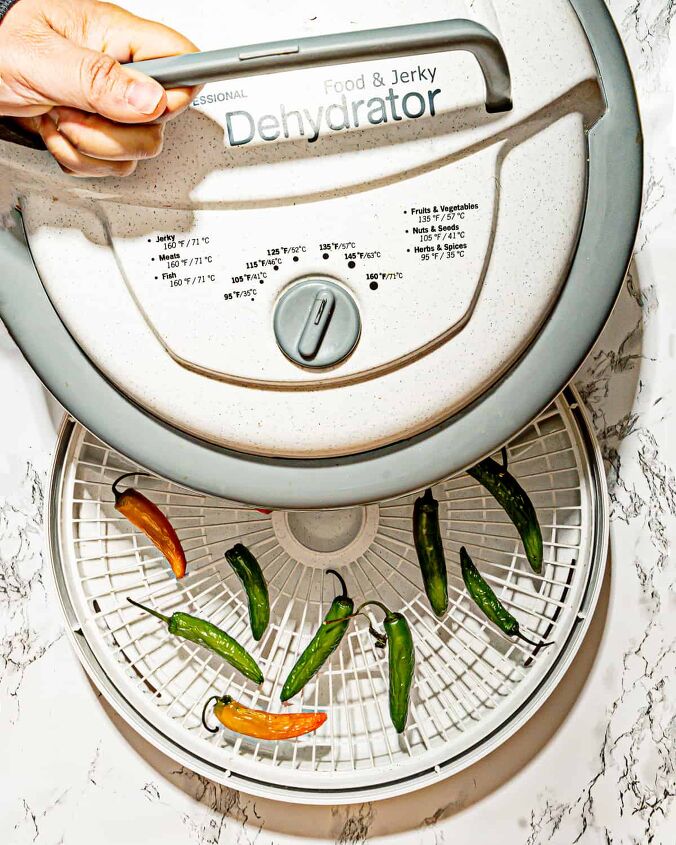 how to dry habanero peppers, person adding dehydrator cover to habanero peppers