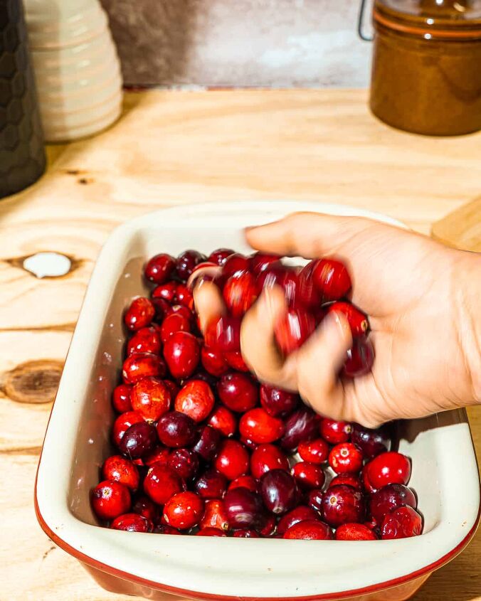honey fermented cranberries, person holding cranberries over a small baking dish