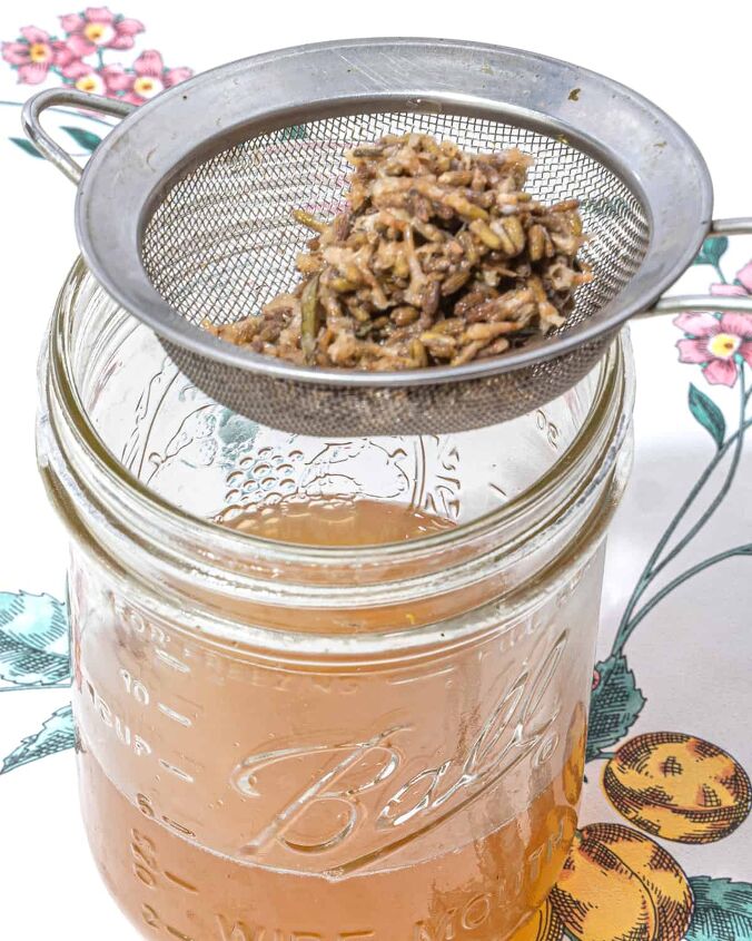 honey lavender lemonade, person straining lavender buds and water through a fine mesh strainer into a mason jar
