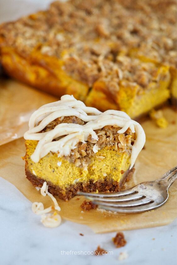 pumpkin cheesecake bars recipe with streusel topping, Fork bite removed from Pumpkin Streusel bar on parchment paper with rest of bars in background