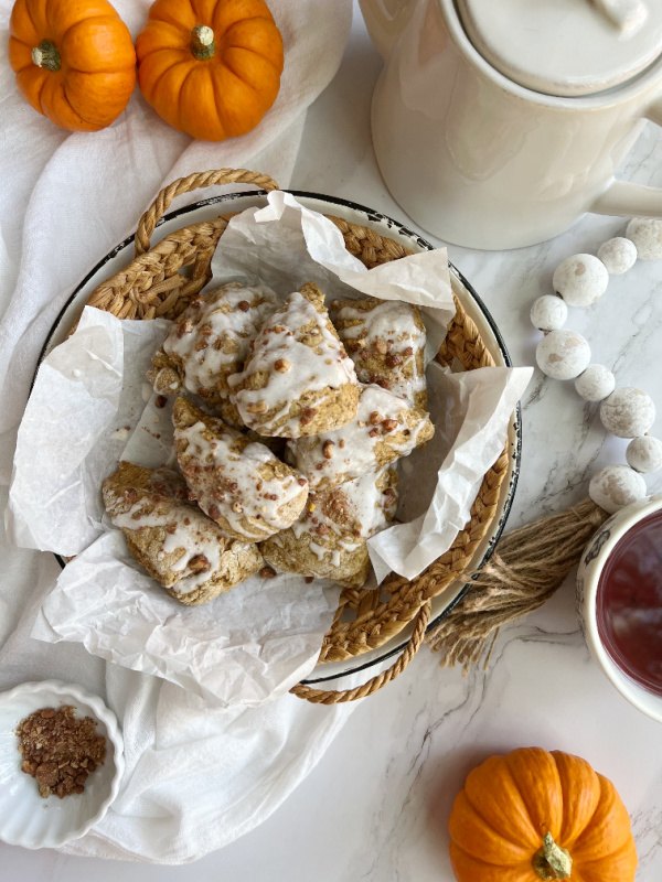 pumpkin scones with glaze and candied pecans, pumpkin scones in a shallow basket with a white teapot and orange pumpkins
