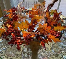 the best cider, A gorgeous Crate and Barrel punch bowl on a round glass table with clear glass cups Surrounding the punch bowl is a garland of silk leaves that are illuminated with white lights