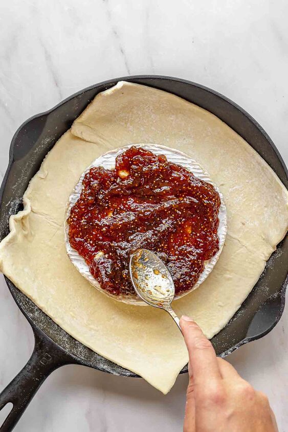 baked brie with fig jam, Fig jam being spread on top of brie with a spoon