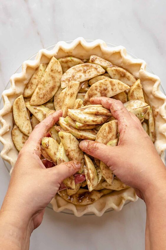 dutch caramel apple pie with crumb topping, Hands adding spiced apple slices to a pie crust