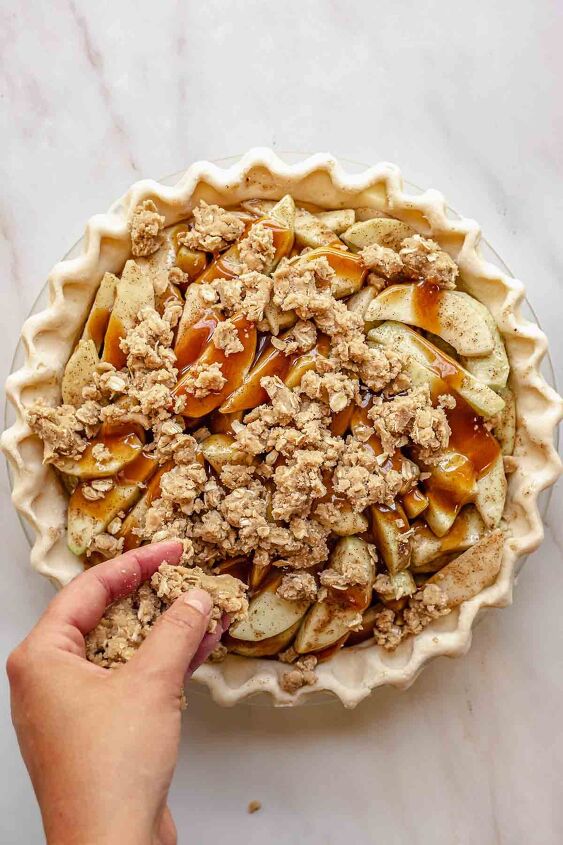 dutch caramel apple pie with crumb topping, A hand adds crumb topping to the apples