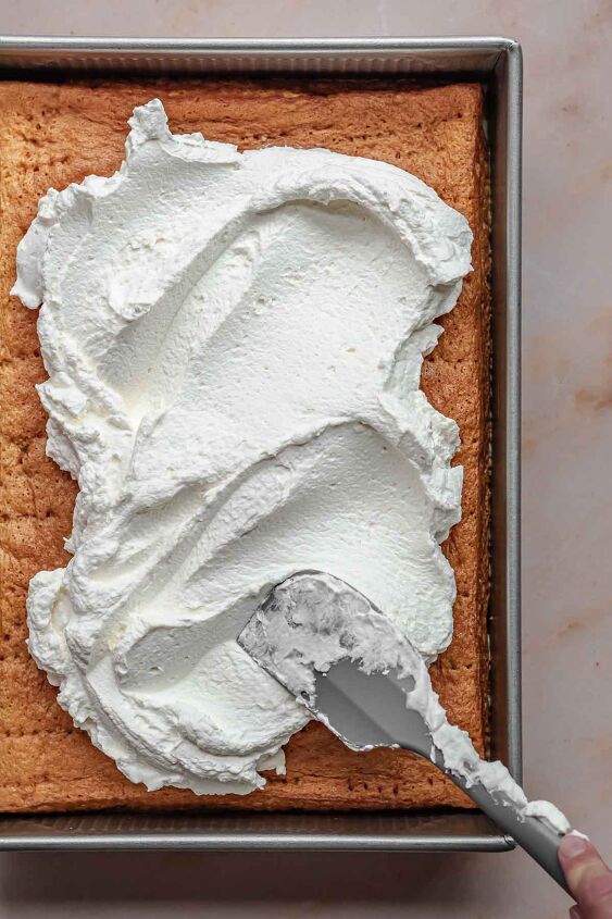 caramel tres leches cake, A spatula spreads fresh whipped cream onto the cake