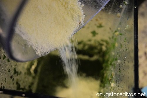 Parmesan cheese being poured into a blender with kale pesto