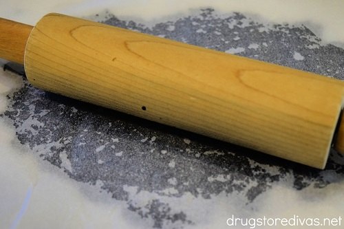 A rolling pin rolling out Oreo cookie crumbles under parchment paper