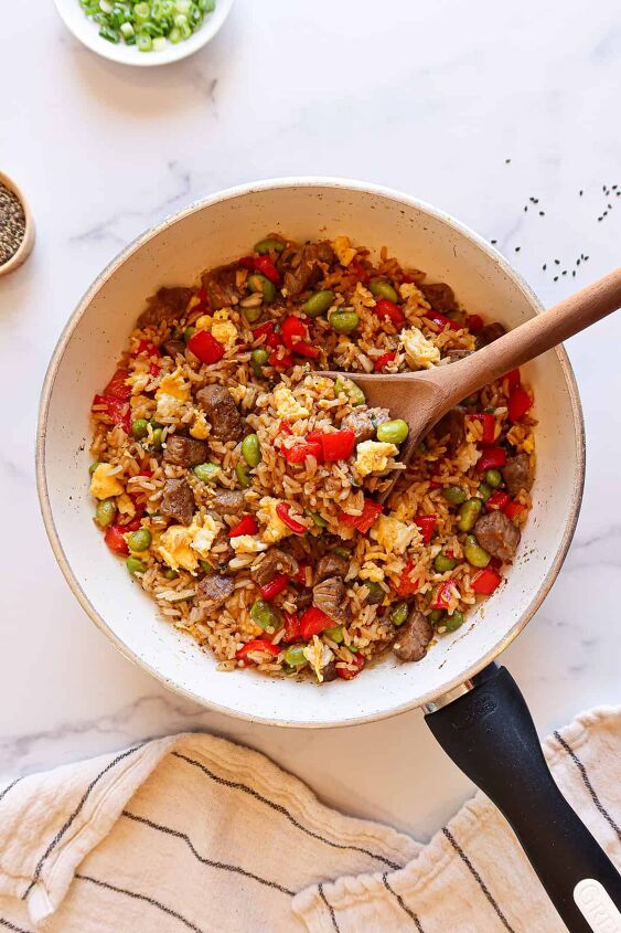 spectacular steak fried rice recipe, Fried rice with steak in a white skillet with a wooden serving spoon