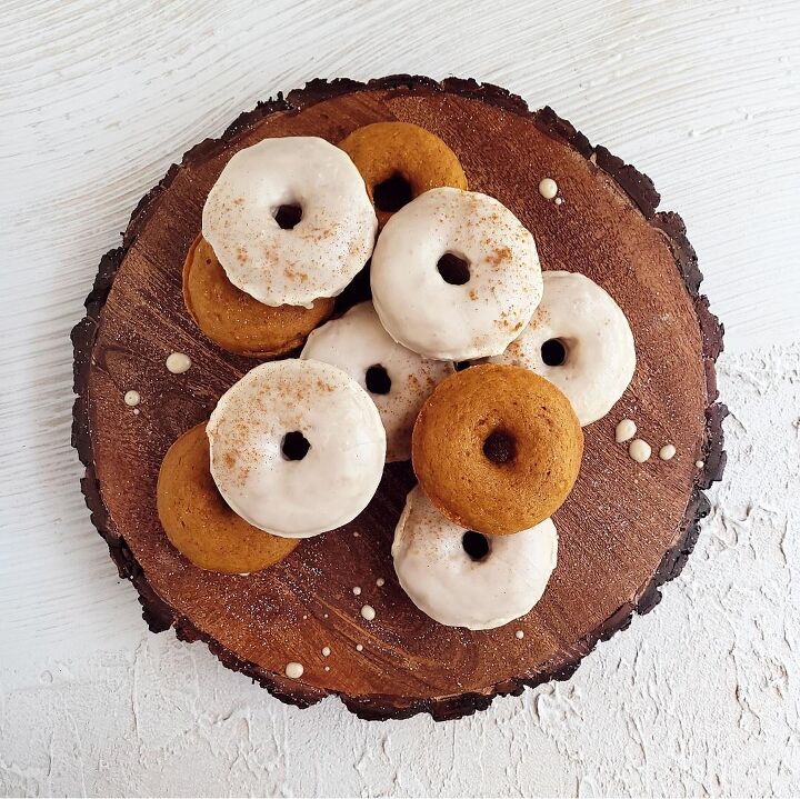 pumpkin donuts, functional image glazed pumpkin donuts on a wooden circle with bark around the edges background is white abstract baked donuts are stacked on top of each other some have glaze and some do not for contrast