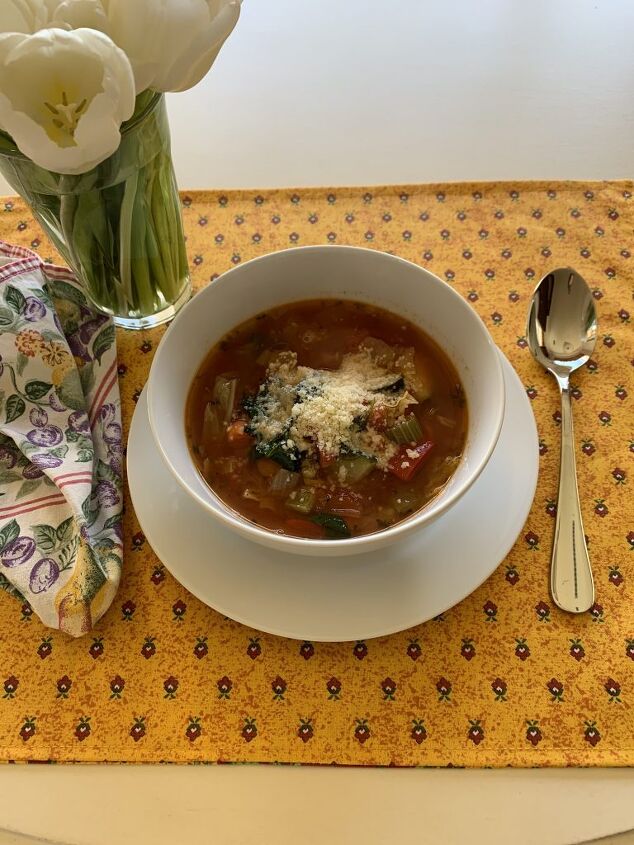 delicious ten vegetable soup, A white ceramic bowl of ten vegetable soup The cowl is on a yellow print placemat with a pretty print napkin and a vase filled with white tulips