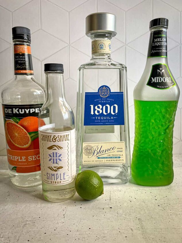halloween margarita witches brew cocktail happy honey kitchen, Ingredients needed to make witches brew Halloween margarita A fresh lime bottles of tequila midori triple sec and simple syrup are on a concrete table