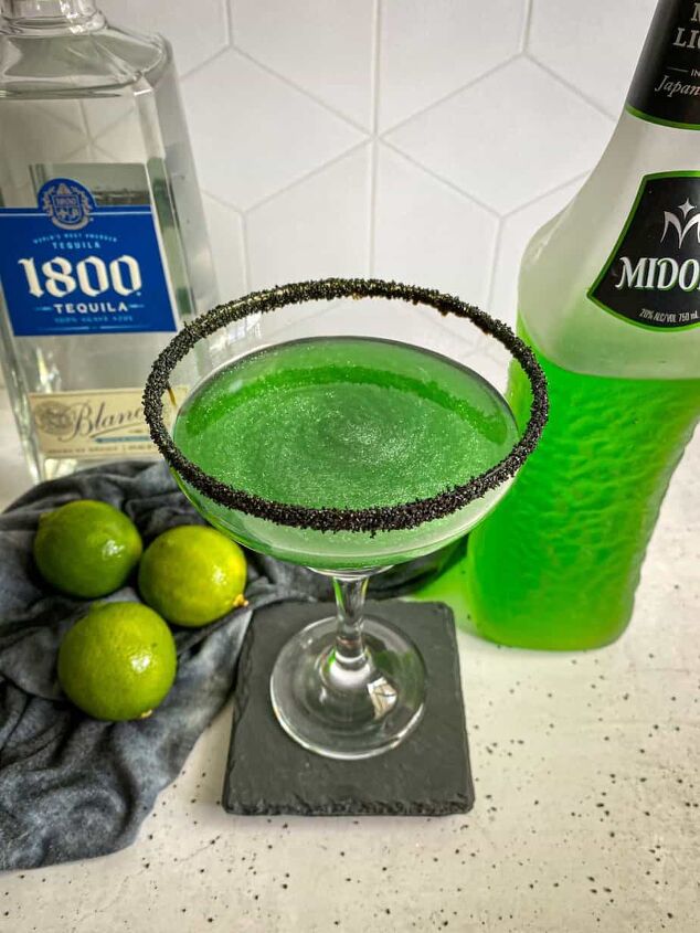 halloween margarita witches brew cocktail happy honey kitchen, Halloween margarita with a black sugar rim A bottle of midori melon liqueur and tequila are in the background with three limes