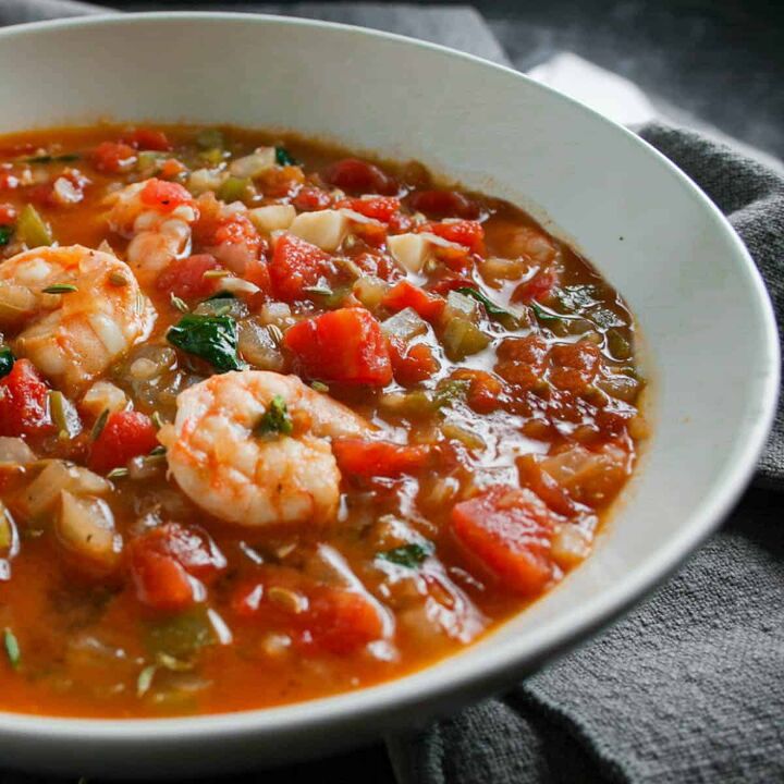 30 minute fennel and tomato seafood cioppino stew, Close up photograph of seafood cioppino in a white bowl with a grey napkin