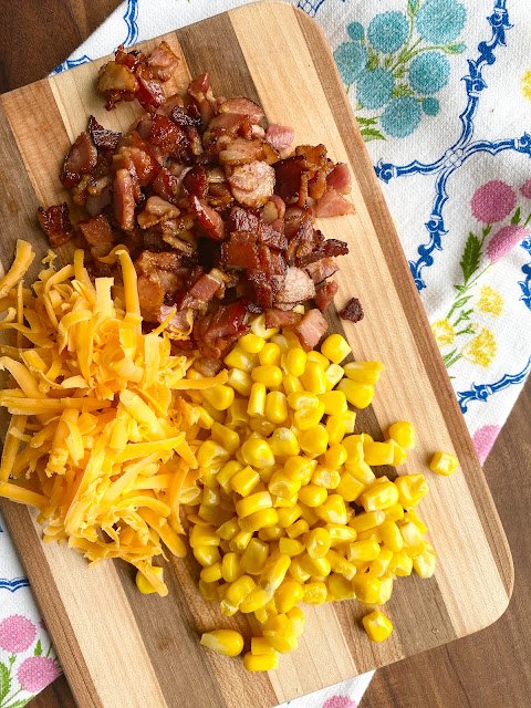 cheesy corn bacon potato chowder, Wooden cutting board with bacon cheddar cheese and corn on a flowered tea towel