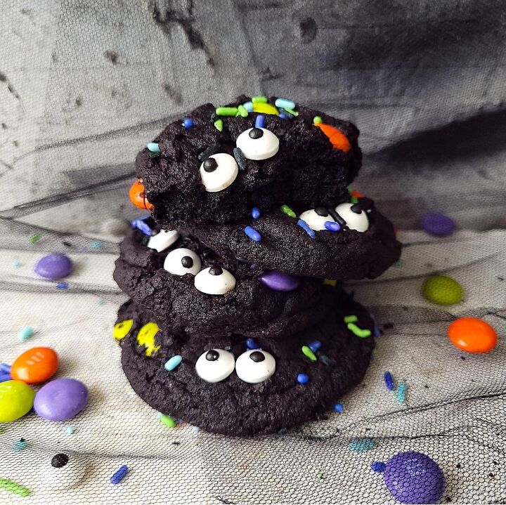 chocolate halloween cookies, functional image m m halloween cookies with candy eyes and halloween sprinkles 4 cookies stacked on top of each other on black tulle with a distressed gray background