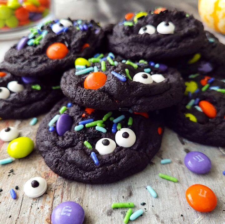 chocolate halloween cookies, functional image chocolate halloween cookies side view of black cookies piled on top of each other cookies are garnished with candy eyes halloween m ms and halloween sprinkles
