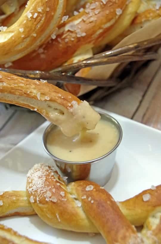 close up of homemade German pretzel being dunked in beer cheese dip