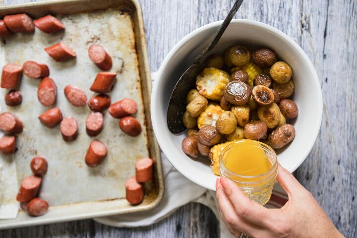 sausage sheet pan dinner, Butter sauce being poured over potatoes and corn next to a tray of sausage