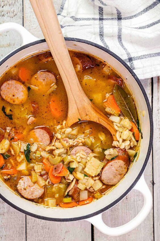 barley sausage vegetable soup with bacon graupensuppe, Barley sausage soup in a white Dutch oven on a white wooden table and wooden spoon