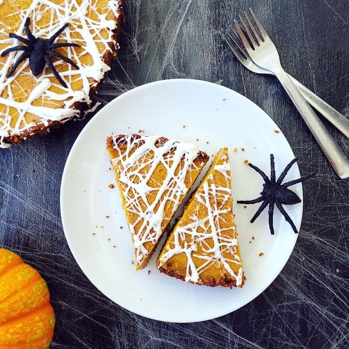 marshmallow spiderweb pumpkin tart, functional image pumpkin tart topped with a white marshmallow spiderweb two slices cut on a shared white plate with a big black spider top down background is black image is styled with a mini pumpkin two forks and the uncut portion of the tart in the upper left corner