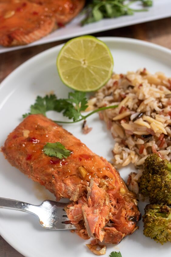 asian air fryer salmon, A round white dinner plate topped with a piece of salmon The salmon has a fork taking a piece from it There s wild rice and broccoli next to the salmon on the plate with a half of a lime and cilantro