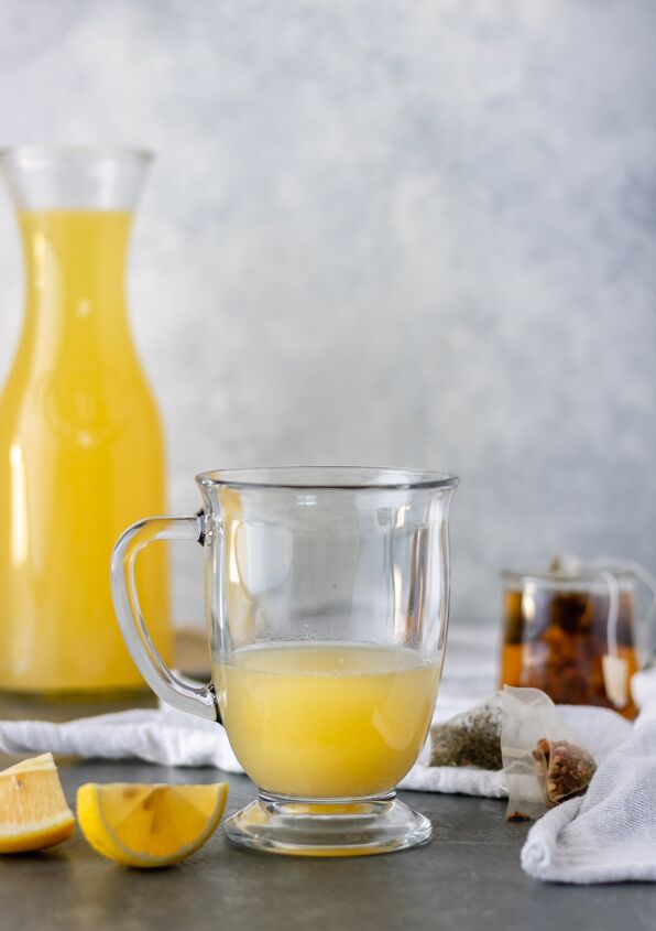 hot honey ginger tea with homemade lemonade, A glass mug of steamed lemonade surrounded by lemon slices tea bags and a large pitcher of homemade lemonade