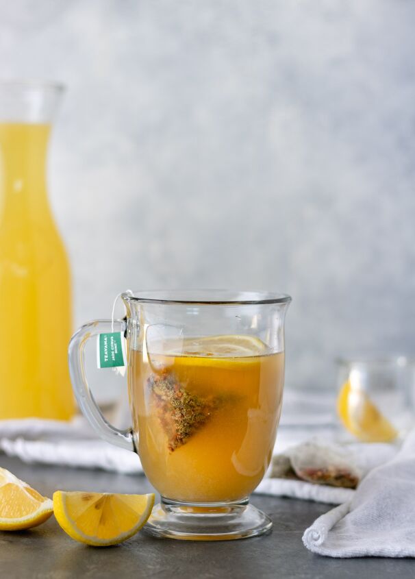 hot honey ginger tea with homemade lemonade, A full glass mug of Hot Honey Ginger Tea surrounded by lemon slices tea bags and a large pitcher of homemade lemonade