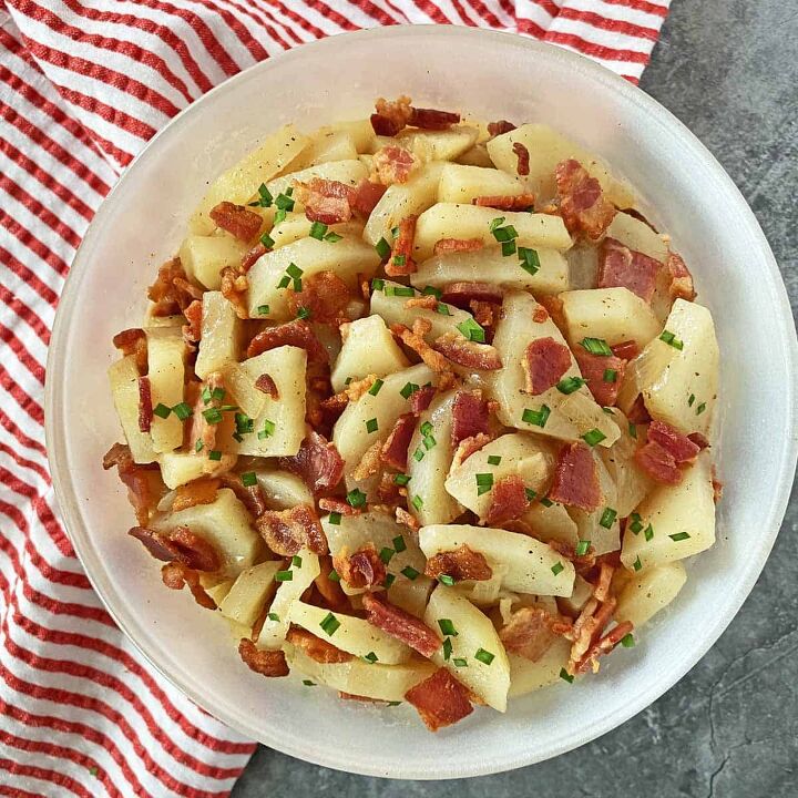 warm potato salad recipe with bacon, Warm potato salad with bacon garnished with chives in a white bowl on a read and white striped napkin