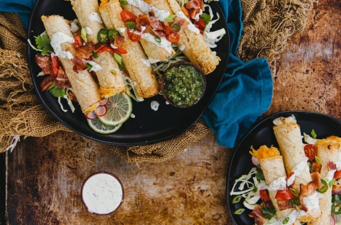 air fryer cheesy potato taquitos, homemade air fryer potato stuffed taquitoes piled onto plated with a variety of toppings