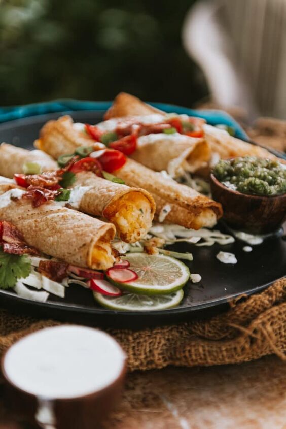 air fryer cheesy potato taquitos, Plate with several air fried potato stuffed taquitos a cream in the foreground and topped with quick pico