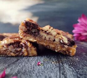 chocolate pecan pie bars, functional image chocolate chip pecan pie cookie bars side view of two bars cut into squares the left bar is sitting diagonally on the left bar there is a purple mum flower in the back right corner and the backdrop is blueish gray abstract