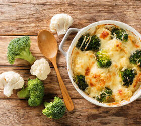 broccoli cauliflower alfredo casserole, wooden board with a round casserole of broccoli cauliflower alfredo casserole with raw broccoli and cauliflower florets on the side with a wooden spoon top view
