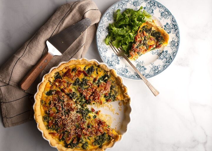 spinach and bacon quiche, Whole quiche with one slice placed on a plate with a green salad