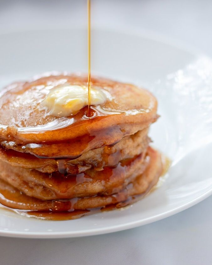 Up close side view of a stack of whole wheat pancakes on a white plate with maple syrup
