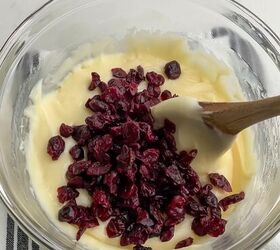 cranberry pecan christmas fudge recipe, wooden spoon stirring dried cranberries into white chocolate fudge mixture