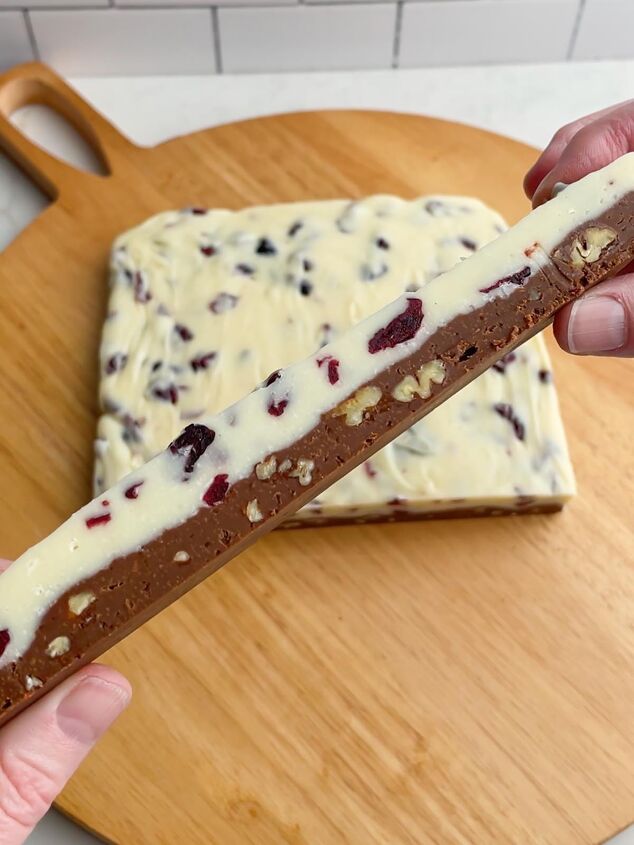 cranberry pecan christmas fudge recipe, hands holding up a bar of fudge to show the white and semi sweet chocolate layers