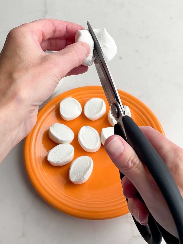 chocolate marshmallow cookies, hand holing scissors snipping a marshmallow in half over a plate of already cut marshmallows