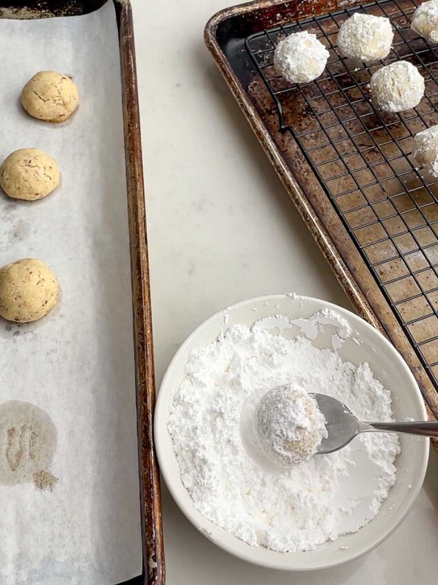 mexican wedding cookies, spoon lifting a rolled Mexican Christmas cookie out of a bowl of powdered sugar