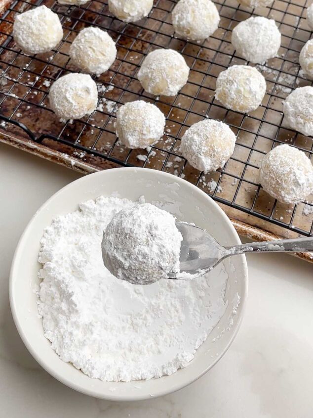 mexican wedding cookies, spoon lifting a rolled Mexican Christmas cookie out of a bowl of powdered sugar