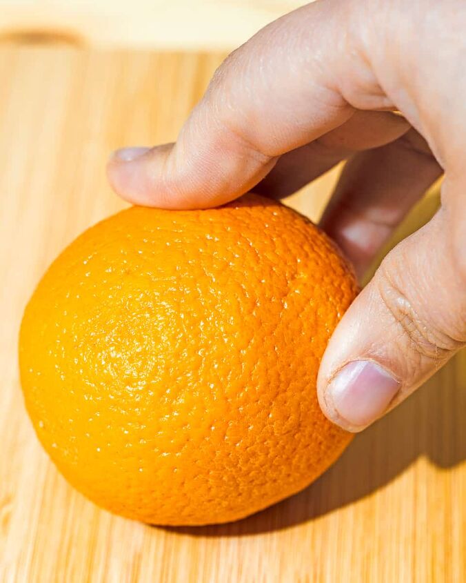 easy oven dried orange slices, person holding down orange on a wooden board
