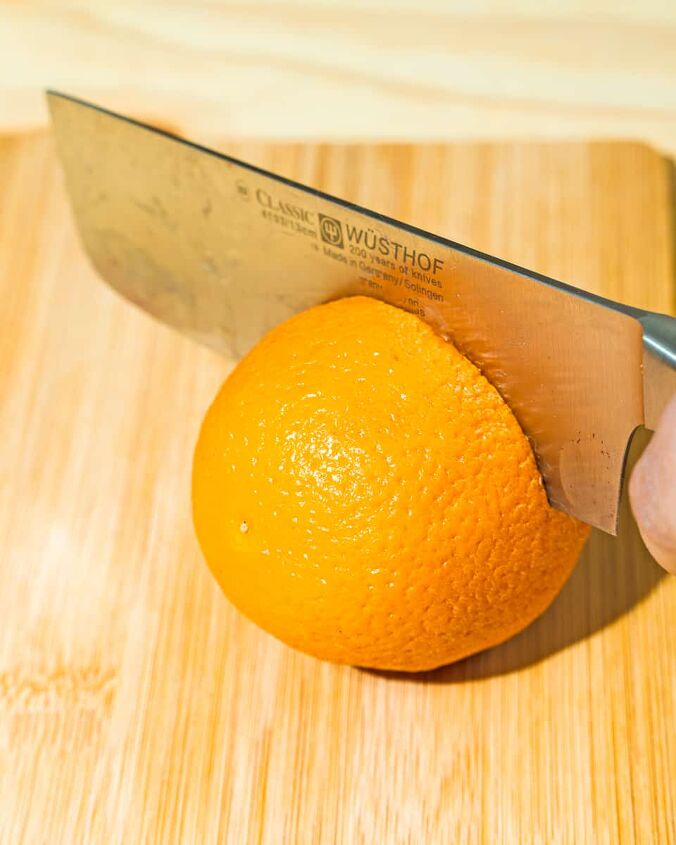 easy oven dried orange slices, person cutting orange with knife on a wooden board