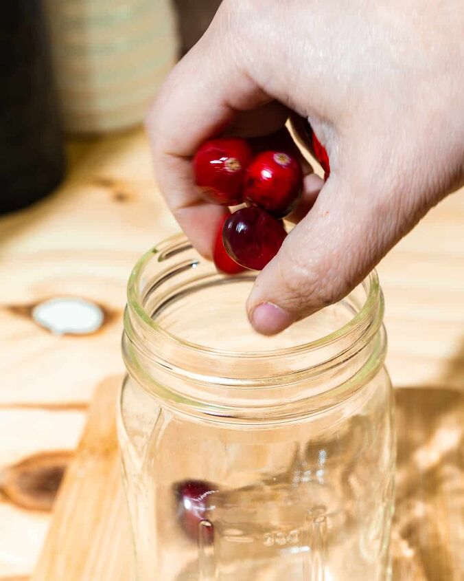 christmas old fashioned, person placing cranberries in mason jar