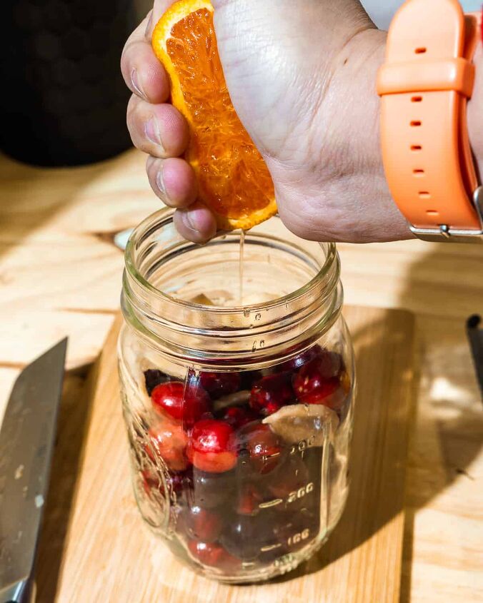 christmas old fashioned, person squeezing juice into orange in mason jar