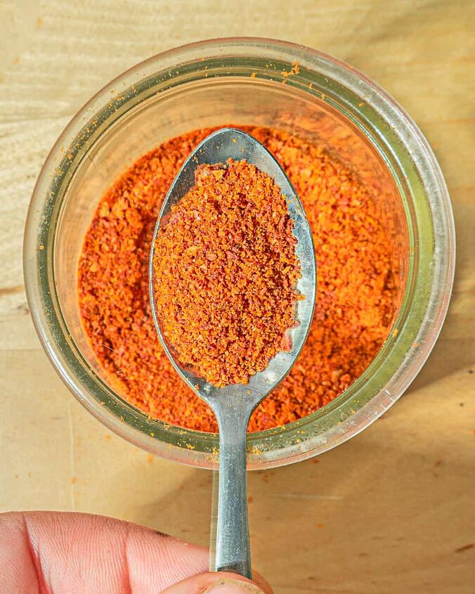 dehydrated tomato powder recipe, person holding spoon with red tomato powder over a glass jar of powder