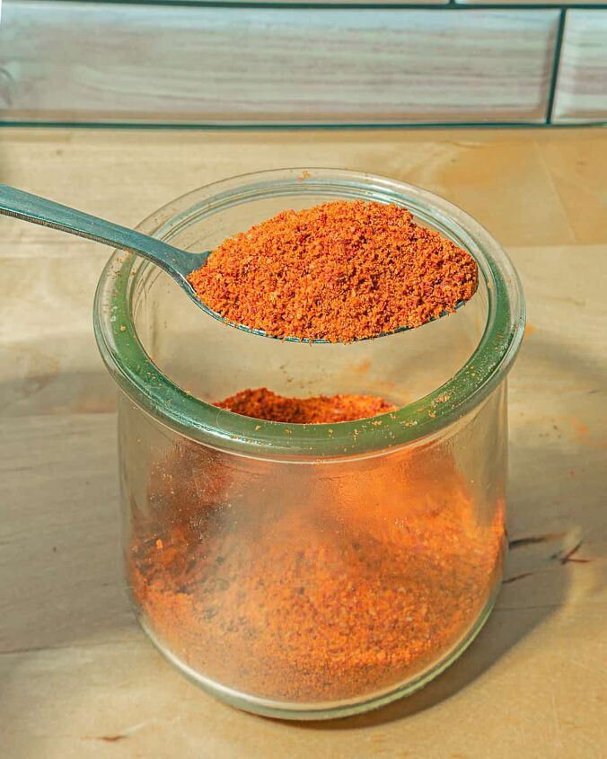 dehydrated tomato powder recipe, person holding spoon with red tomato powder over a glass jar of powder