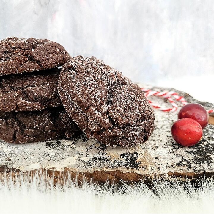chocolate molasses crinkle cookies, functional image stack of three chocolate molasses crinkle cookies with a fourth cookie leaning on the stack side view on a distressed wood surface styled with cranberries and red and white holiday twine